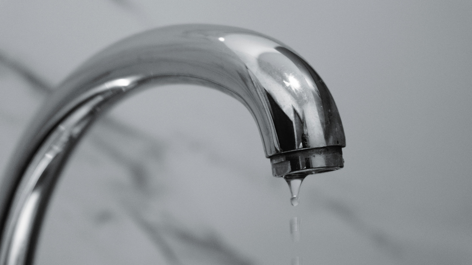 Close-up of a chrome faucet with a water droplet dripping from the tip