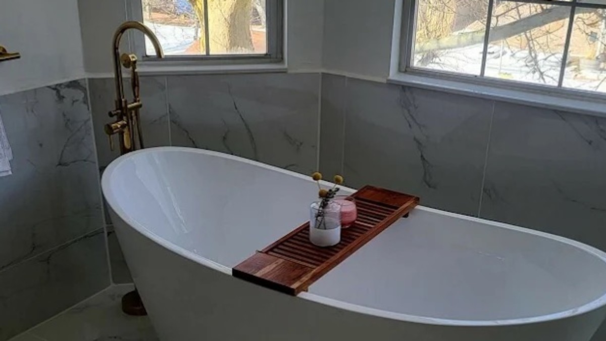 White freestanding bathtub with a wood bath tray in a marble bathroom